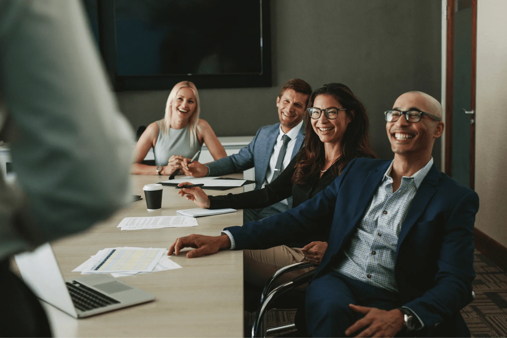 A group of professionals smile at a speaker in a boardroom